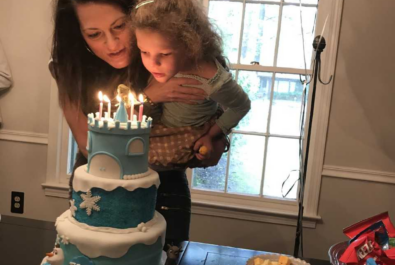 mother holding child while she blows the candles of a castle cake out